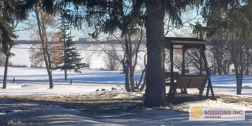 trees covered in snow and a wooden swing overlooking a lake
